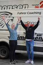 Zwei Mitarbeiter der Fahrschule Simonsen stehen jubelnd vor einem Transporter.